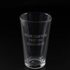 A clear glass from the "Pair of Pint Glasses - Your Custom Text/Logo Here" set is depicted against a black background, with the text "YOUR CUSTOM TEXT OR LOGO HERE" etched onto its surface. The empty glass stands upright, perfectly centered in the image. This elegant piece is ideal for displaying your custom text or logo and can be paired with another pint glass for added impact.