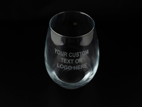 Transparent glass from the "Pair of Wine Glasses - Your Custom Text/Logo Here" set, featuring an engraving that reads "YOUR CUSTOM TEXT OR LOGO HERE" against a black background, ideal for personalized wine glasses.