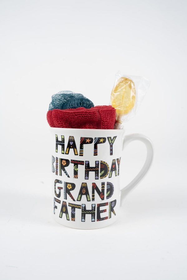 A white Happy Birthday Grandfather Mug with Free Food Certificate displays "Happy Birthday Grandfather" in colorful, patterned letters. The gift pack inside the mug includes a red and green knit item and a yellow, round, wrapped candy, all set against a plain white background.