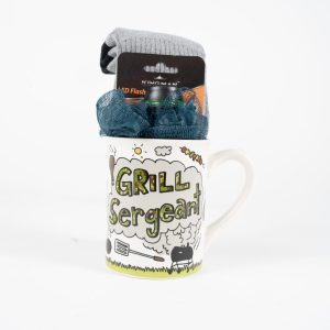 A white ceramic Grill Sergeant Mug Gift Basket with colorful illustrations, filled with gray socks and teal scrubbies, on a white background, includes a complimentary free food certificate.