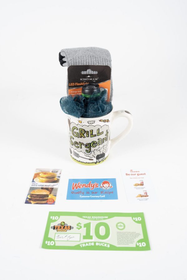 A Grill Sergeant Mug Gift Basket with Free Food Certificate, featuring a white mug brimming with a pair of socks, a blue loofah, and a flashlight, sits proudly on a white background. Surrounding the mug are various gift cards and free food certificates from McDonald's, Wendy's, Texas Roadhouse, and an elegant dine-in restaurant. This delightful gift basket makes for the perfect present!