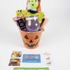 The Halloween Pail with Free Food Certificate includes a witch-themed plush toy, a green towel adorned with black bat designs, a jar candle, body lotion, and an assortment of snacks. Additionally, it features trade bucks and free food certificates from Wendy's, Chick-fil-A, and McDonald's.