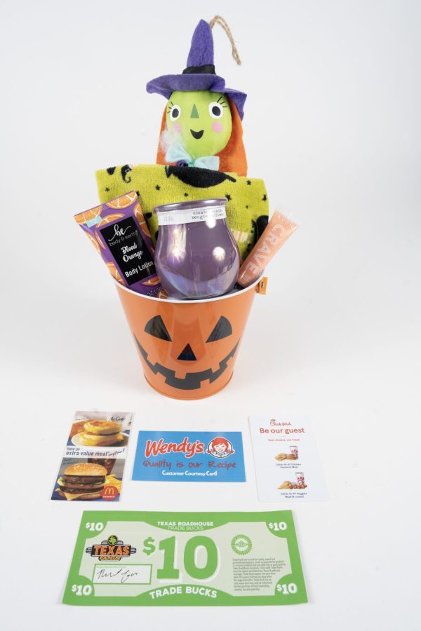 The Halloween Pail with Free Food Certificate includes a witch-themed plush toy, a green towel adorned with black bat designs, a jar candle, body lotion, and an assortment of snacks. Additionally, it features trade bucks and free food certificates from Wendy's, Chick-fil-A, and McDonald's.