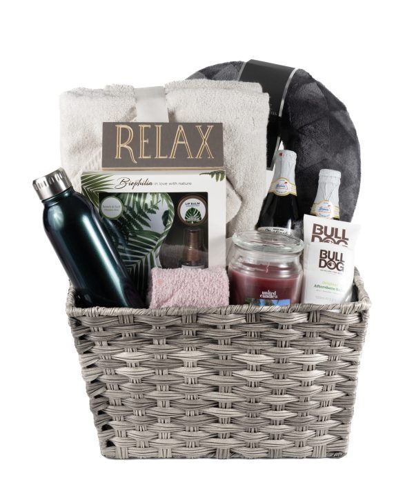 The His & Hers Spa Gift Basket - Large includes a grey wicker basket containing a black water bottle, pink towel, rolled white towel, box labeled "Relax," sparkling beverage bottle, jar candle, Bulldog skincare products, and a grey and black blanket—the ultimate spa gift for both him and her.