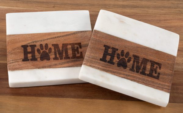 The Pair of Pet Square Coasters - Home, featuring marble coasters with wooden inlays, sit on a wooden surface. Each inlay showcases the word "HOME" with a paw print replacing the letter "O," creating a rustic and pet-friendly home decor aesthetic.