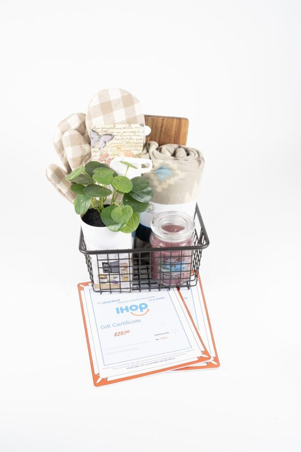 An IHOP Kitchen & Home Basket, which includes kitchen mitts, a rolled towel, a small potted plant, a cutting board, and a scented candle, sits on a white surface. Beneath the basket are multiple $50 IHOP gift certificates.