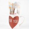 A white "For You Love Mug Gift Basket with Free Food Certificate," adorned with a large red heart and the words "FOR YOU" written inside, holds various beauty products. Visible items include packaged cosmetics and a nail polish bottle. The background is plain white.