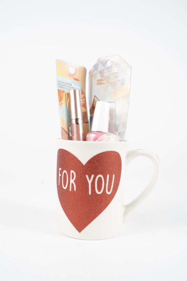 A white "For You Love Mug Gift Basket with Free Food Certificate," adorned with a large red heart and the words "FOR YOU" written inside, holds various beauty products. Visible items include packaged cosmetics and a nail polish bottle. The background is plain white.