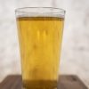 On a wooden surface rests a clear glass brimming with golden, carbonated liquid—presumably beer. The light background is softly blurred, drawing attention to the sparkling drink with bubbles dancing their way to the top. A Pair of Pint Glasses - Buckeye Team awaits a celebratory toast in honor of Buckeye Team’s victory.