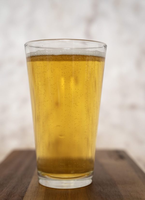 On a wooden surface rests a clear glass brimming with golden, carbonated liquid—presumably beer. The light background is softly blurred, drawing attention to the sparkling drink with bubbles dancing their way to the top. A Pair of Pint Glasses - Buckeye Team awaits a celebratory toast in honor of Buckeye Team’s victory.