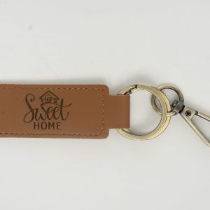 A tan leather keychain from our "Custom Key Chain - Laser engraved on one or Both Sides" collection, featuring the phrase "Home Sweet Home" laser engraved. This keychain includes a metal ring and a silver-colored clip, ideal for showcasing your sentiment on both sides.