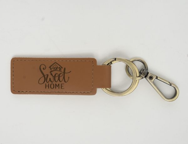 A tan leather keychain from our "Custom Key Chain - Laser engraved on one or Both Sides" collection, featuring the phrase "Home Sweet Home" laser engraved. This keychain includes a metal ring and a silver-colored clip, ideal for showcasing your sentiment on both sides.