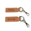 Two keychains from the "Home Sweet Home Key Chains - Set of 2" are shown with rectangular leather tags. The top keychain's tag reads "Ashly" while the bottom keychain's tag reads "Kevin." Each leather tag features attached metal rings and clasps, making them perfect for adding a touch of personalized charm to your home.