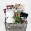 An Adult Gambling Night Basket filled with various items: red and white checkered oven mitts, two rolls of chunky white yarn, a small green potted plant, a red candle in a glass jar, a floral-patterned notebook, and other small household and decorative items perfect for an adult's relaxing night at home.