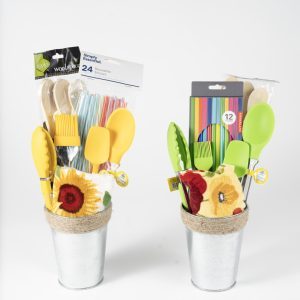 The Adult Gambling Night Basket features two metallic pails filled with kitchen essentials and biodegradable striped straws. One pail contains yellow and green silicone utensils, while the other includes an assortment of yellow and green utensils, colored pencils, and an elegant touch suitable for a sophisticated adult evening. Both pails are adorned with decorative cloth flowers and wooden utensils.