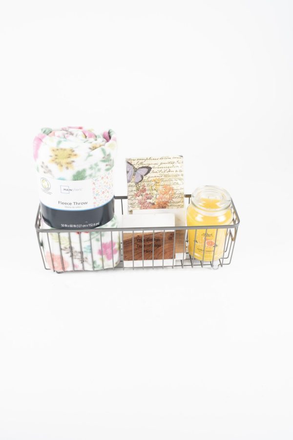 A wire basket contains a rolled-up fleece throw with a floral design, a floral-themed card, custom coasters, and a yellow glass candle. The items are arranged neatly against a white background, making it an ideal Personalized Kitchen & Home Gift Basket with 2 Custom Coasters for any occasion.