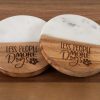 A Pair of Less People More Dogs Round Coasters, each featuring round wooden construction with elegant white marble inlays, are displayed on a wooden surface. Ideal for dog lovers, both coasters showcase the engraved phrase "LESS PEOPLE MORE DOGS" along with a charming small paw print graphic.