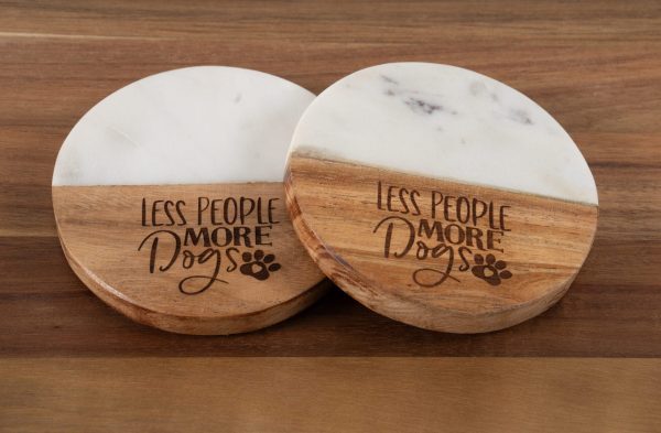 A Pair of Less People More Dogs Round Coasters, each featuring round wooden construction with elegant white marble inlays, are displayed on a wooden surface. Ideal for dog lovers, both coasters showcase the engraved phrase "LESS PEOPLE MORE DOGS" along with a charming small paw print graphic.