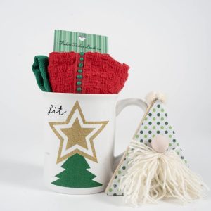 A festive scene with the Christmas Glitter Tree Mug Gift Basket, featuring a white ceramic mug adorned with a gold star and glitter tree. The mug is filled with red and green socks, while beside it stands a small gnome decoration sporting a polka-dotted green hat and a fluffy white beard, completing the Christmas charm.