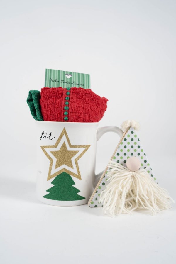 A festive scene with the Christmas Glitter Tree Mug Gift Basket, featuring a white ceramic mug adorned with a gold star and glitter tree. The mug is filled with red and green socks, while beside it stands a small gnome decoration sporting a polka-dotted green hat and a fluffy white beard, completing the Christmas charm.