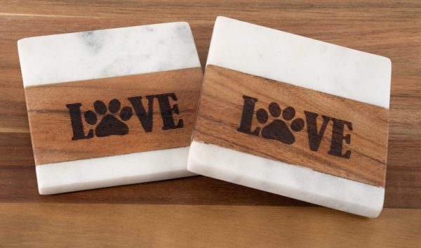 The Pair of Pet Square Coasters - Love features two square coasters with white marble tops and bottoms, accented by a wooden band in the middle. The wooden section is engraved with the word "LOVE," where the “O” is creatively replaced by a paw print, symbolizing affection for pets. These charming pet-themed coasters are perfect for placing on any wooden surface.