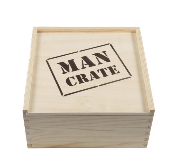 The Man Crate Gift Box features a wooden crate with the words "MAN CRATE" stenciled in black on the top lid. It boasts a natural wood finish and dovetail joints at the corners, with the lid slightly lifted to reveal its contents.