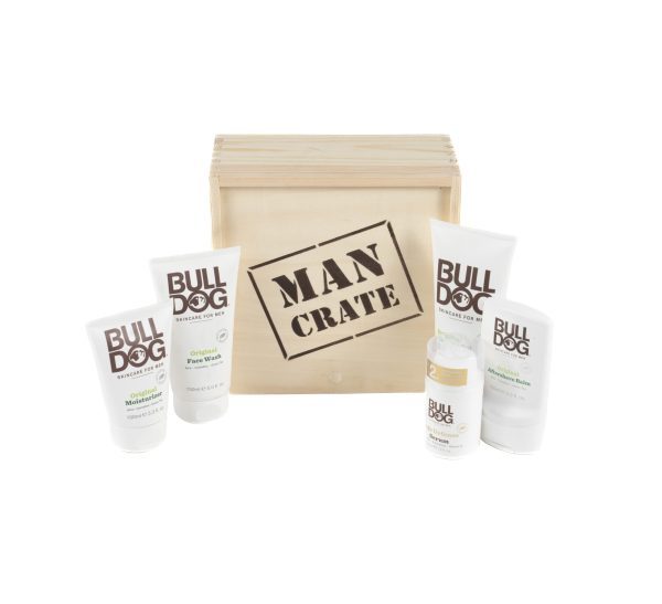 A wooden crate labeled "Man Crate Gift Box" is surrounded by various skincare products from the brand Bulldog. The gift box includes face washes, moisturizers, and shaving items, all in white packaging with the brand and product names clearly visible.