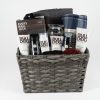 The Adult Gambling Night Basket contains various men's grooming products, such as lotion, deodorant, body wash, and moisturizer from Bulldog brand. It also includes an Every Man Jack grooming kit. Additionally, the basket features a rolled gray towel, a small checkered blanket, and a brown sponge—perfect for any adult's daily routine.