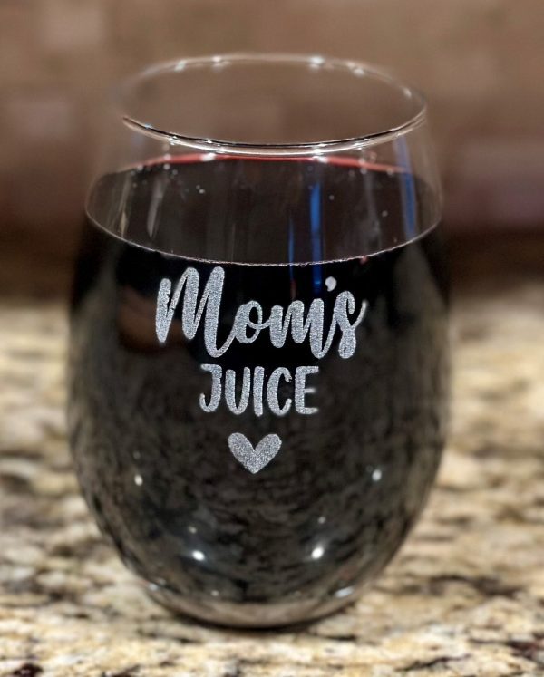 A stemless Mom's Juice Wine Glass filled with a dark red liquid, likely wine, stands on a granite countertop. The front of the wine glass displays the text "Mom's Juice" with a small heart symbol below it.