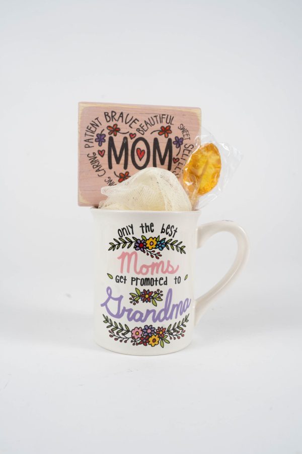 The Promoted to Grandma Mug Gift Basket with Food Certificate includes a white Grandma Mug decorated with vibrant floral patterns and the phrase "Only the best Moms get promoted to Grandma." Inside, there is a wooden sign that reads "MOM," surrounded by affirmations such as "patient," "brave," and "beautiful." Also included are a bath sponge, a packet, and a Food Certificate—an ideal addition to any heartfelt gift basket.