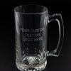 The Glass Mug - Single is a clear glass mug featuring an inscription on the front that reads "YOUR CUSTOM TEXT OR LOGO HERE." This single glass mug comes with a simple, sturdy handle and a patterned base, set against a dark background.