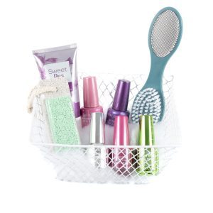 The Manicure/Pedicure Basket includes a white wire basket that holds a tube of Sweet Pea lotion, a green pumice stone with an attached rope, an assortment of colorful nail polishes, and a dual-sided foot scrubbing brush with a teal handle. Perfect for both pedicures and manicures, the basket is lined with white tissue paper.