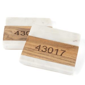 Two rectangular blocks resembling a pair of square coasters, primarily white with a marble-like pattern and a smooth wooden texture in the middle, featuring an engraved zip code "43017." The background is plain white. Product: Pair Square Coasters - Choose any Zip Code.