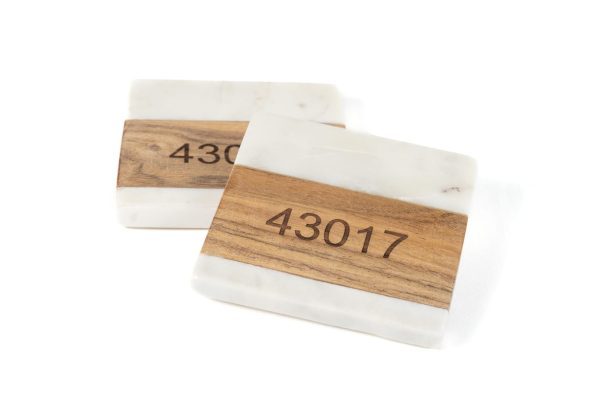 Two rectangular blocks resembling a pair of square coasters, primarily white with a marble-like pattern and a smooth wooden texture in the middle, featuring an engraved zip code "43017." The background is plain white. Product: Pair Square Coasters - Choose any Zip Code.