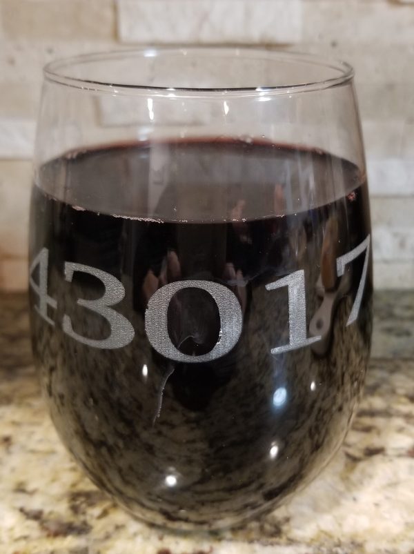 A pair of **Pair of Wine Glasses - Choose any Zip Code**, each etched with the zip code "43017" in large, clear fonts, are placed on a granite countertop. The background showcases a light stone backsplash with subtle patterns.