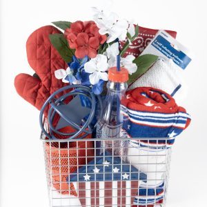 Introducing the Adult Gambling Night Basket: a wire basket filled with a red oven mitt, artificial red, white, and blue flowers, a blue jar opener, a clear water bottle with a red lid and straw, red and white dish towels, a rolled-up striped towel, and a small box adorned with an American flag design.