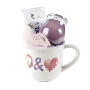 The Peace & Love Mug Gift Basket with Free Food Certificate features a vibrant mug embellished with colorful peace and heart symbols on the front, containing a pink loofah, a jar of lavender-scented candle in purple, and a tube of lavender salt scrub. This gift basket is thoughtfully arranged to provide an inviting and relaxing presentation.