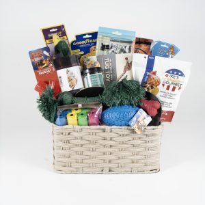 The Adult Gambling Night Basket is a beige woven basket filled with various dog toys and treats, perfect for an adult night in with your furry friend. Items include dog snacks, chew toys, a rope toy, a rubber ball, and packages of different dog-friendly foods and treats. The basket is neatly arranged with colorful packaging and toys visible.