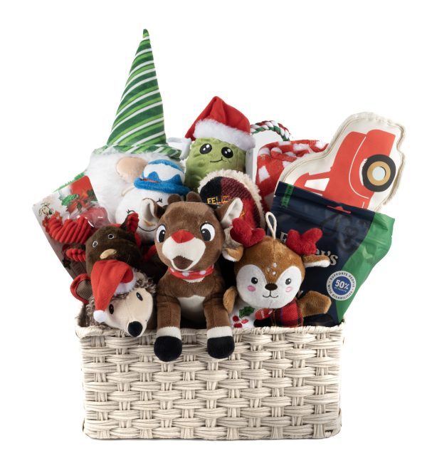 The Holiday Dog Pet Basket - Large is a festive gift basket brimming with Christmas-themed stuffed toys, including reindeer, Santa hats, a plush character in a green elf hat, and a toy truck. Wrapped presents and green packaging add to the cheerful display. The light-colored woven basket brings joy to any home or pet this season.