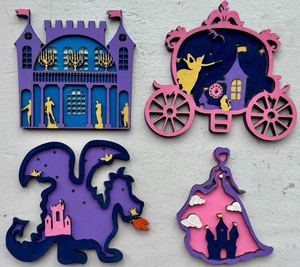 The Princess Craft Kit features four vibrant wooden cutouts: a castle with lit chandeliers, a carriage with a dancing figure, a dragon breathing fire near a tower, and a princess's dress with a castle. The intricate designs burst with blue, purple, pink, and yellow hues.