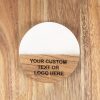 The "Pair Round Coasters - Your Custom Text/Logo Here" features a round, wooden, flat design with a smooth finish and a white top section. The bottom wooden portion is engraved with the text "YOUR CUSTOM TEXT OR LOGO HERE." These personalized coasters are placed on a wooden surface.