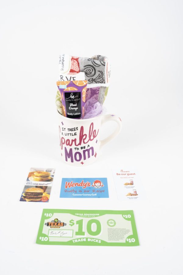 Introducing the Sparkle Mom Mug Gift Basket with Free Food Certificate, which includes a lovely mug inscribed with "It takes a little sparkle to be a mom," colorful socks, body lotion, and free food certificates from McDonald's, Wendy's, and "Trade Bucks." Additionally, a white envelope containing an unidentified card accompanies this thoughtful gift basket.