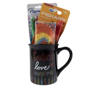 A "Teach Love Mug Gift Basket with Free Food Certificate," featuring colorful text that says "Teach love inspire" on a black mug, holds various school supplies, including a pack of Fiskars kids scissors, a pack of Paper Mate InkJoy pens, and a tie-dye-patterned item, all sticking out from the mug.