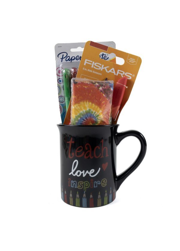 A "Teach Love Mug Gift Basket with Free Food Certificate," featuring colorful text that says "Teach love inspire" on a black mug, holds various school supplies, including a pack of Fiskars kids scissors, a pack of Paper Mate InkJoy pens, and a tie-dye-patterned item, all sticking out from the mug.