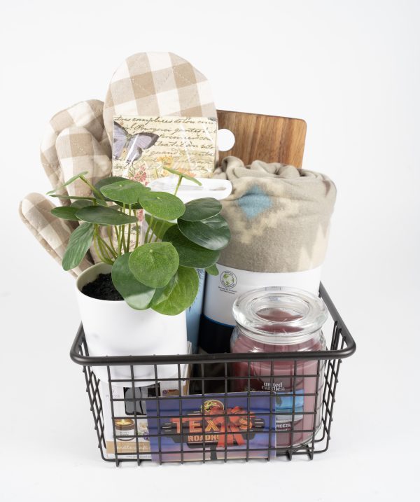 A Texas Road House Kitchen & Home Basket, containing $75 in Texas Roadhouse Certificates, features a metal basket with a potted plant, plaid oven mitts, a small wooden board, a rolled blanket, a large red candle, and a white candle. The items are all neatly arranged against a white background.