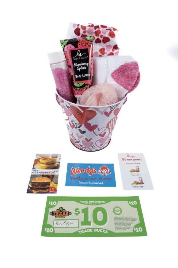 A Valentine's Day Hearts Mug with a love heart design includes items such as a tube of body lotion, a pink bath pouf, and socks adorned with heart patterns. In front are various gift cards worth $10 each for popular food places like McDonald’s, Wendy's, Chick-fil-A, and Texas Roadhouse—perfect for Valentine's Day.