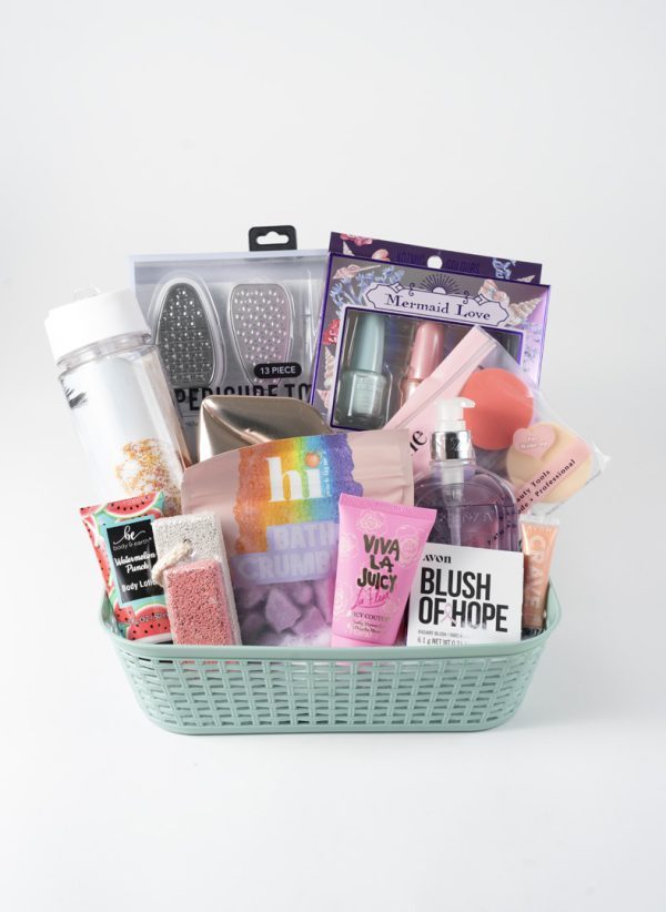 An Adult Gambling Night Basket contains various pampering items, including a water bottle, bath crumbles, a pair of foot files, a mermaid-themed nail polish set, a bottle of Blush of Hope liquid, a bar of soap, a lip scrub, and a Viva La Juicy travel fragrance.