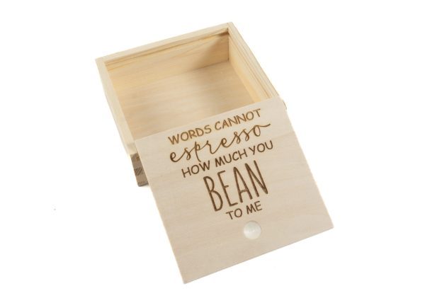 A small, open light-colored wooden gift box from the "Gift Box - Words Cannot Express How Much You Bean to Me" collection with the lid propped against it. The lid features an engraving in a mix of cursive and uppercase letters that reads, "WORDS CANNOT espresso HOW MUCH YOU BEAN TO ME.