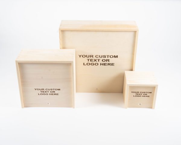 Three "Wooden Gift Box - Small Planter or Bakery Size" items of different dimensions are displayed against a white background. Each box features the phrase "YOUR CUSTOM TEXT OR LOGO HERE" printed on its front, indicating space for personalized designs or logos. These boxes, resembling charming small planters, are arranged from largest to smallest.