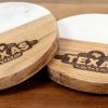 Two round coasters with white marble tops are pictured on a wooden surface. Both personalized coasters feature the Texas Roadhouse logo, part of the "Pair Round Coasters - Your Custom Text/Logo Here" product collection, engraved in the wood section.